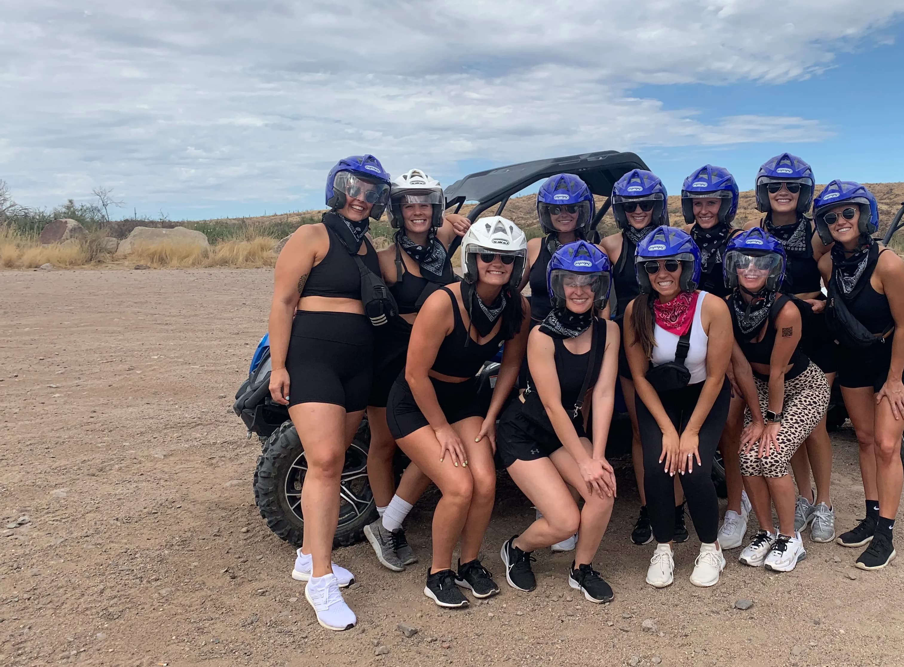 Group of women posing with helmets on and a sand buggy in the background